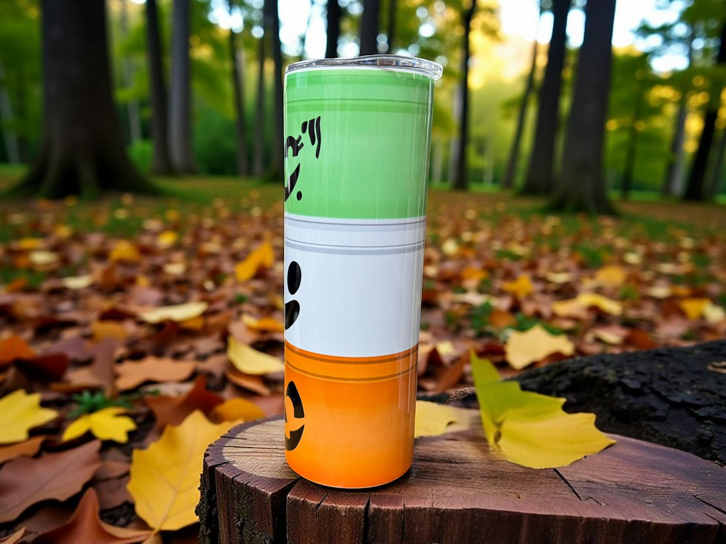 Tumbler with green, white, and orange design on a wooden stump in a forest setting