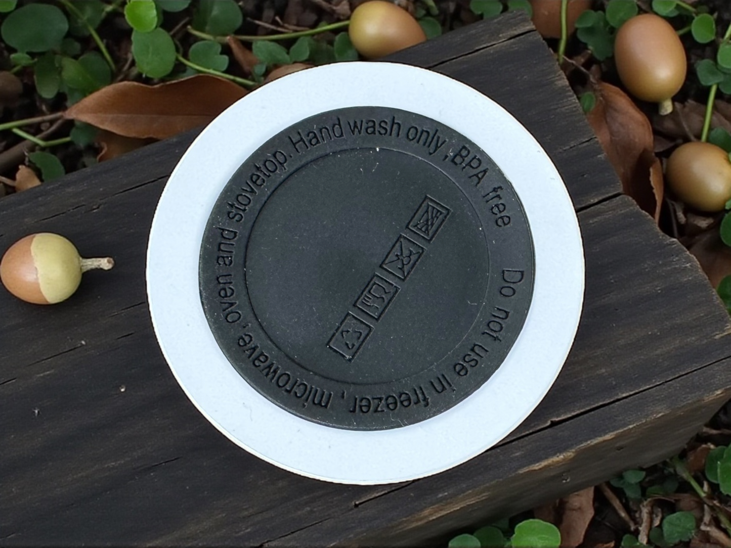 Round black rubber piece on the bottom of a tumbler on a wooden surface with leaves in the background