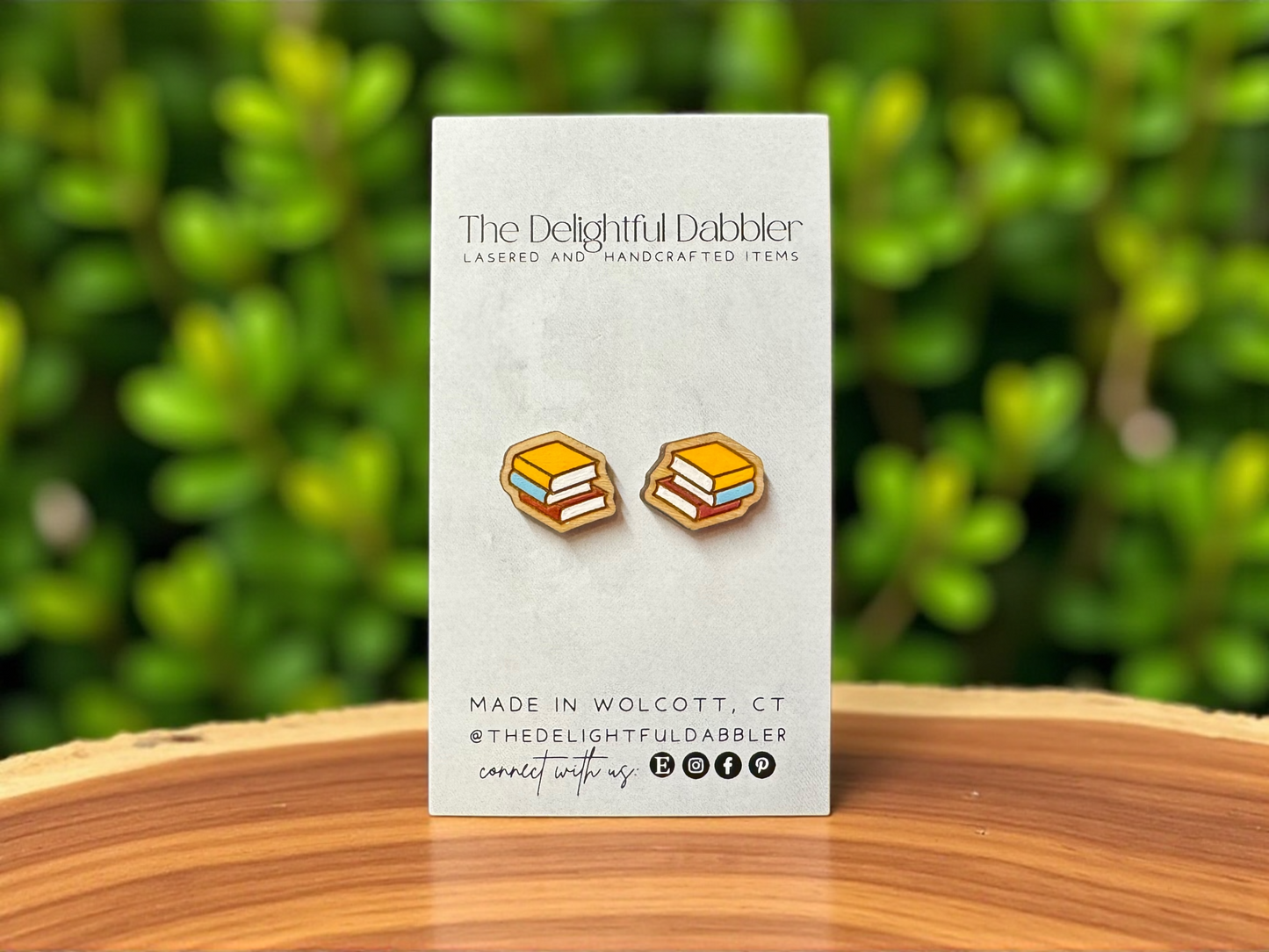 Earring card with stacked book wood stud earrings on a wooden surface and green foliage background