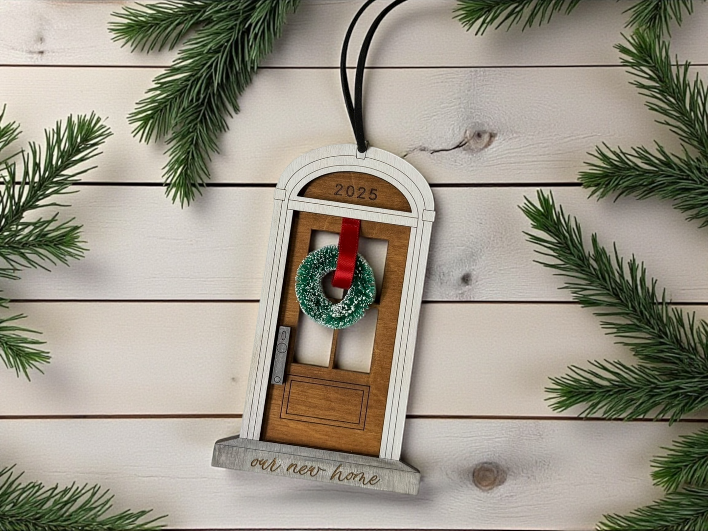 Decorative ornament with a wreath, red ribbon, and 'our new home' text on a wooden background with pine branches.