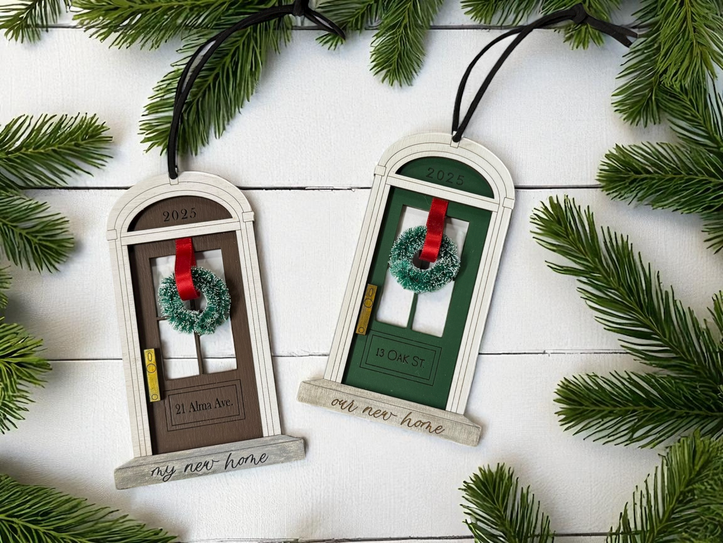 Decorative door-shaped ornaments with wreaths on a white wooden background with greenery.